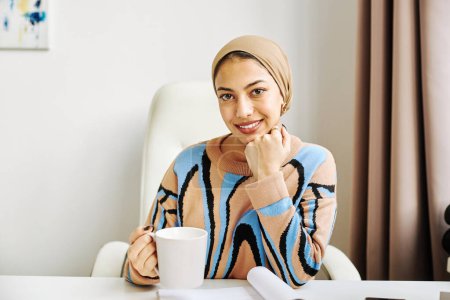 Téléchargez les photos : Portrait minimal de l'élégante femme musulmane en tant que femme patron souriant à la caméra dans le bureau - en image libre de droit