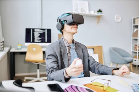 Foto de Retrato de vista lateral de un joven sonriente con auriculares VR en la oficina mientras trabaja en un proyecto de realidad inmersiva - Imagen libre de derechos