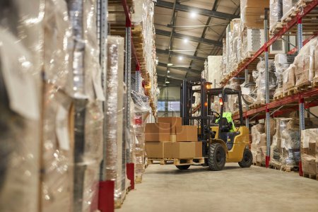 Photo for Background image of warehouse interior with forklift carrying boxes, copy space - Royalty Free Image