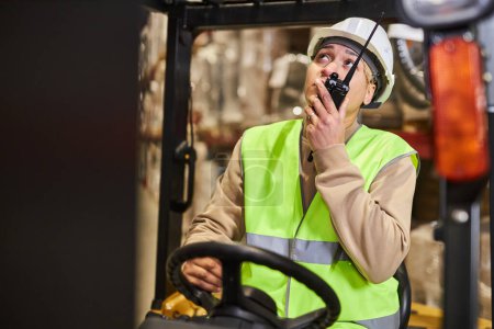 Photo for Portrait of female worker wearing hardhat while operating forklift truck in warehouse and talking to portable radio, copy space - Royalty Free Image