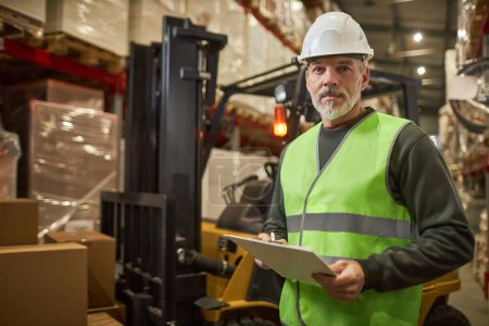 Photo for Waist up portrait of bearded worker wearing hardhat and looking at camera in warehouse, copy space - Royalty Free Image
