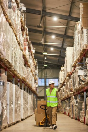 Photo for Vertical portrait of female worker carrying boxer in warehouse and walking towards camera - Royalty Free Image