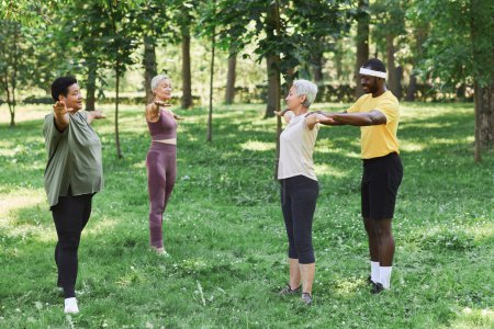 Photo for Side view of three senior women working out outdoors in green park with trainer assisting - Royalty Free Image