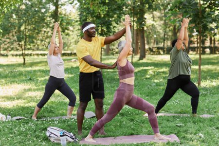 Téléchargez les photos : Portrait complet de l'entraîneur sportif aidant groupe de femmes âgées profitant du yoga en plein air dans le parc - en image libre de droit