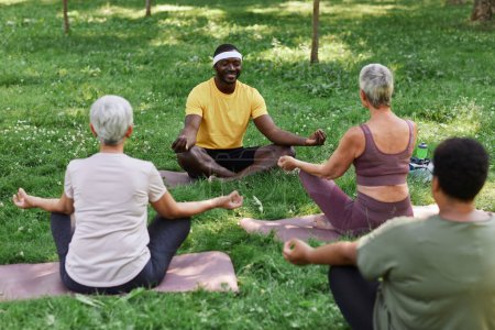 Téléchargez les photos : Portrait complet de l'entraîneur de yoga masculin avec groupe de femmes âgées profitant de la méditation en plein air - en image libre de droit