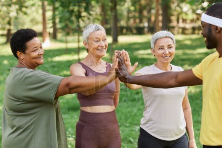 Téléchargez les photos : Groupe de femmes âgées actives High Five avec formateur après avoir apprécié l'entraînement en plein air dans le parc - en image libre de droit