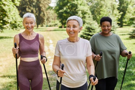 Photo for Group of active senior women walking with poles towards camera outdoors and smiling - Royalty Free Image