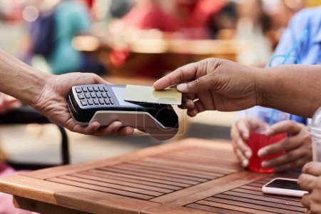 Téléchargez les photos : Gros plan de la femme âgée noire payant avec une carte de crédit dans un café extérieur - en image libre de droit