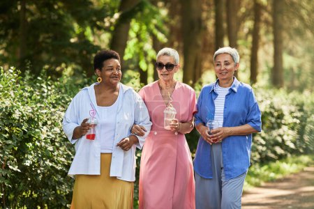 Photo for Group of fashionable senior women walking towards camera in park and holding drinks - Royalty Free Image