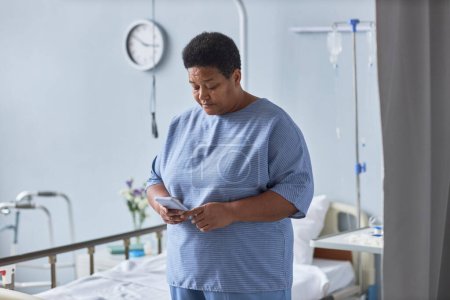Téléchargez les photos : Portrait taille haute de la femme âgée noire en utilisant un smartphone dans la chambre d'hôpital - en image libre de droit