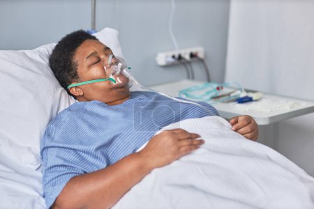 Téléchargez les photos : Portrait de femme âgée noire allongée sur le lit dans la chambre d'hôpital avec support à oxygène dans la récupération covid-19 - en image libre de droit