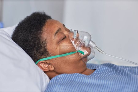 Foto de Vista lateral de la mujer mayor negra durmiendo en la cama en la habitación del hospital con máscara de soporte de oxígeno - Imagen libre de derechos