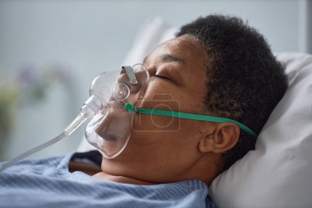 Téléchargez les photos : Vue latérale gros plan de la femme âgée noire dormant sur le lit dans la chambre d'hôpital avec masque de soutien à l'oxygène - en image libre de droit