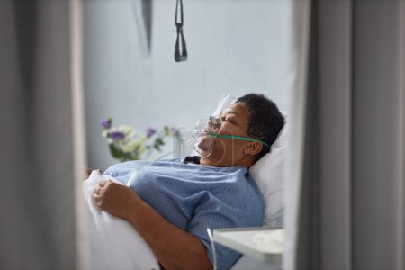 Foto de Retrato de vista lateral mínimo de una mujer afroamericana mayor acostada en la cama en la habitación del hospital con máscara de soporte de oxígeno - Imagen libre de derechos