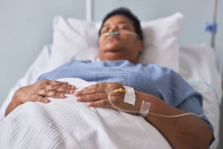 Photo for Black senior woman laying on bed in hospital room with focus on IV tubes in hand, copy space - Royalty Free Image