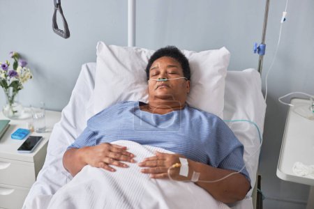 Téléchargez les photos : Femme âgée noire allongée sur le lit dans la chambre d'hôpital avec support IV, vue grand angle - en image libre de droit