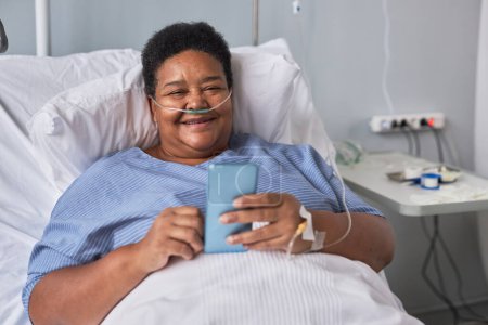 Photo for Portrait of smiling senior woman using phone while laying on bed in hospital room - Royalty Free Image