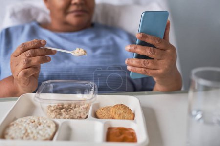 Foto de Primer plano de la mujer mayor negra comiendo comida saludable en bandeja en la sala de recuperación del hospital, espacio para copiar - Imagen libre de derechos