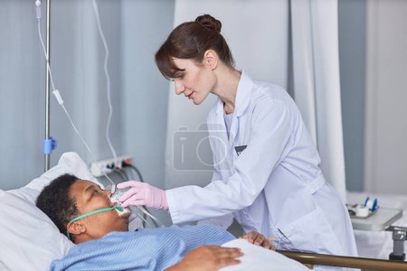 Foto de Retrato de vista lateral de enfermera cuidadora colocando máscara de soporte de oxígeno en paciente mayor en habitación de hospital - Imagen libre de derechos