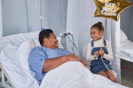 Photo for Portrait of black little girl visiting grandma in hospital room and holding balloons - Royalty Free Image
