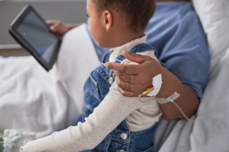 Téléchargez les photos : Femme noire senior avec petite fille utilisant la tablette numérique ensemble dans la chambre d'hôpital pendant les heures de visite - en image libre de droit