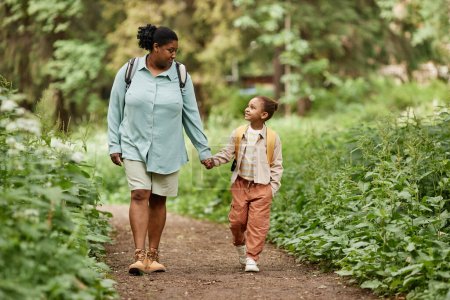 Téléchargez les photos : Portrait complet de mère et fille heureuses marchant sur le sentier de la nature ensemble tenant la main - en image libre de droit