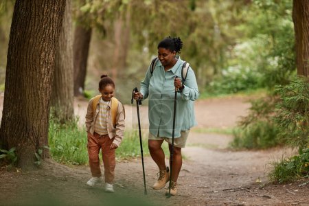 Téléchargez les photos : Portrait complet de mère et fille noires marchant ensemble dans un magnifique sentier forestier, espace de copie - en image libre de droit