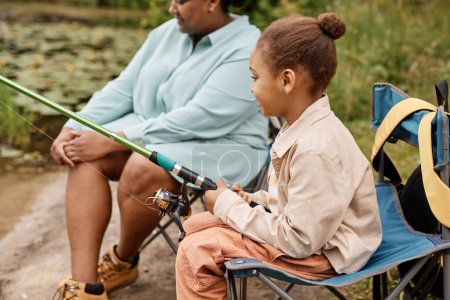 Photo for Side view portrait of black little girl holding fishing rod while enjoying camping with family - Royalty Free Image