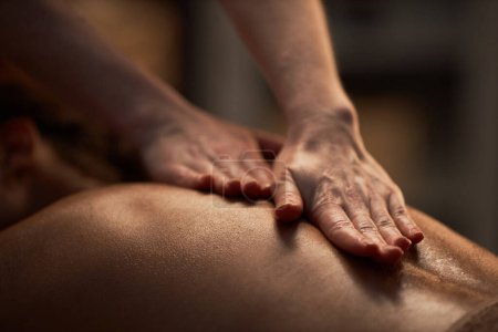 Téléchargez les photos : Mains de masseuse appliquer de l'huile sur le dos de la jeune femme - en image libre de droit
