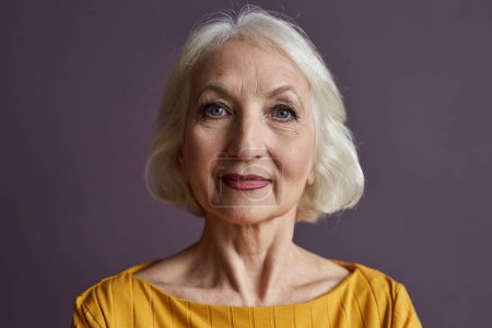 Photo for Minimal close up portrait of of elegant senior woman wearing makeup and looking at camera against dusty purple background - Royalty Free Image