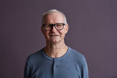Téléchargez les photos : Portrait minimal de l'homme âgé portant des lunettes et souriant à la caméra sur fond violet, espace de copie - en image libre de droit