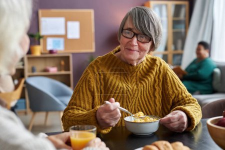 Téléchargez les photos : Portrait d'une femme âgée souriante parlant à un ami pendant le petit déjeuner dans une maison de retraite - en image libre de droit