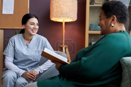 Photo for Portrait of smiling young nurse talking to senior woman in retirement home or assisted living - Royalty Free Image