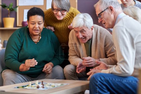 Téléchargez les photos : Groupe de personnes âgées jouant à des jeux de société ensemble à la maison de retraite avec des visages émotionnels - en image libre de droit