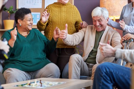 Téléchargez les photos : Portrait d'un homme âgé excité jouant au jeu de société avec un groupe multiethnique d'amis à la maison de retraite - en image libre de droit