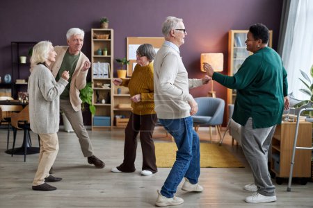 Téléchargez les photos : Vue complète au groupe de personnes âgées dansant à l'intérieur de la maison de retraite et profitant des activités - en image libre de droit