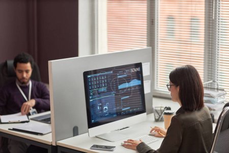 Téléchargez les photos : Vue grand angle de deux employés de bureau au bureau avec cloison, mise au point sur les données à l'écran de l'ordinateur - en image libre de droit