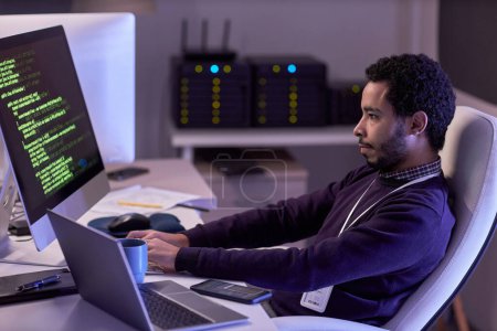 Foto de Retrato de vista lateral del hombre barbudo usando computadoras y escribiendo código en luz de neón - Imagen libre de derechos