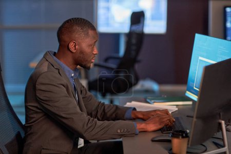 Téléchargez les photos : Portrait latéral du développeur informatique noir portant un costume tout en travaillant sur un projet de sécurité des données au bureau - en image libre de droit