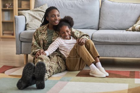 Téléchargez les photos : Heureux enfant passe du temps avec sa mère militaire, ils sont assis sur le sol dans le salon et embrasser - en image libre de droit
