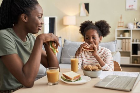 Téléchargez les photos : Mère manger un sandwich avec du jus de fruits avec sa petite fille à la table dans la chambre - en image libre de droit