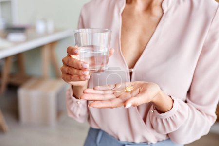 Foto de Primer plano de una joven irreconocible sosteniendo una cápsula vitamínica en la mano con un vaso de agua - Imagen libre de derechos