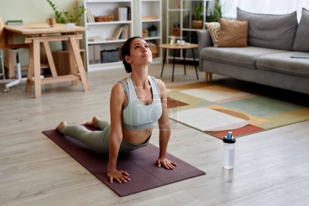 Téléchargez les photos : Portrait de belle jeune femme étirant sur tapis de yoga profiter de l'entraînement à la maison - en image libre de droit