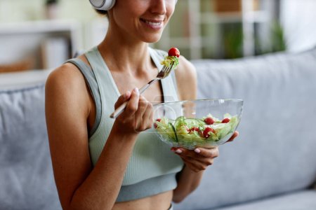 Close up of sportive young woman eating fresh salad while enjoying healthy lifestyle and organic eating at home