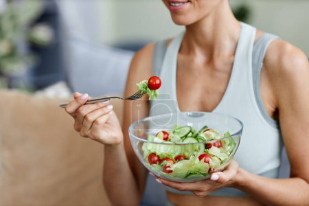 Téléchargez les photos : Gros plan de la femme mangeant de la salade fraîche tout en profitant d'un mode de vie sain et des aliments biologiques à la maison - en image libre de droit