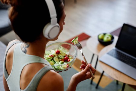 Blick aus der Vogelperspektive auf die sportliche junge Frau, die frischen Salat isst, während sie zu Hause einen gesunden Lebensstil und Bio-Essen genießt