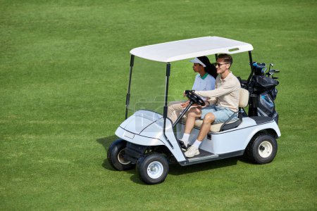 Téléchargez les photos : Vue grand angle au couple sportif conduisant une voiturette de golf sur un terrain vert minimal, espace de copie - en image libre de droit