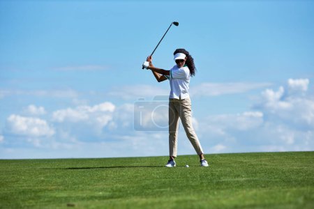 Téléchargez les photos : Portrait complet minimal de jeune femme sportive jouant au golf sur un terrain vert contre le ciel et le club de golf oscillant avec précision, espace de copie - en image libre de droit