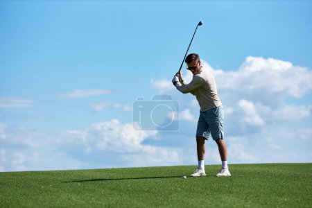 Téléchargez les photos : Portrait complet de l'homme sportif actif balançant club de golf sur le terrain contre le ciel bleu, espace de copie - en image libre de droit