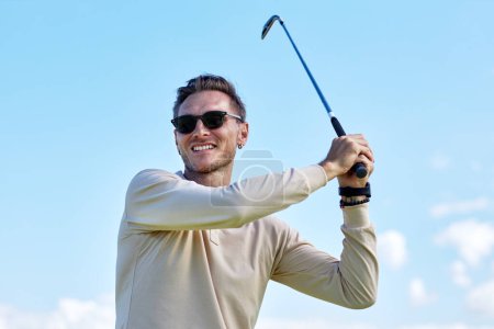 Téléchargez les photos : Portrait taille haute d'un homme sportif souriant jouant au golf et balançant club de golf contre ciel bleu à l'extérieur, espace de copie - en image libre de droit